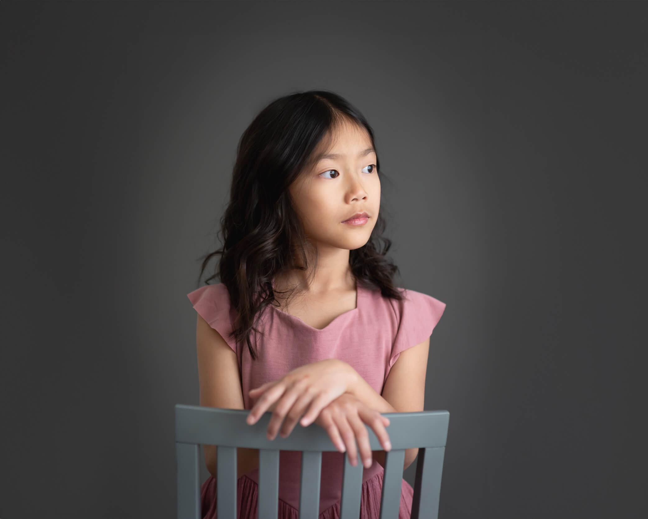 10 year old girl in a blush colored dress sitting backwards on a chair looking away