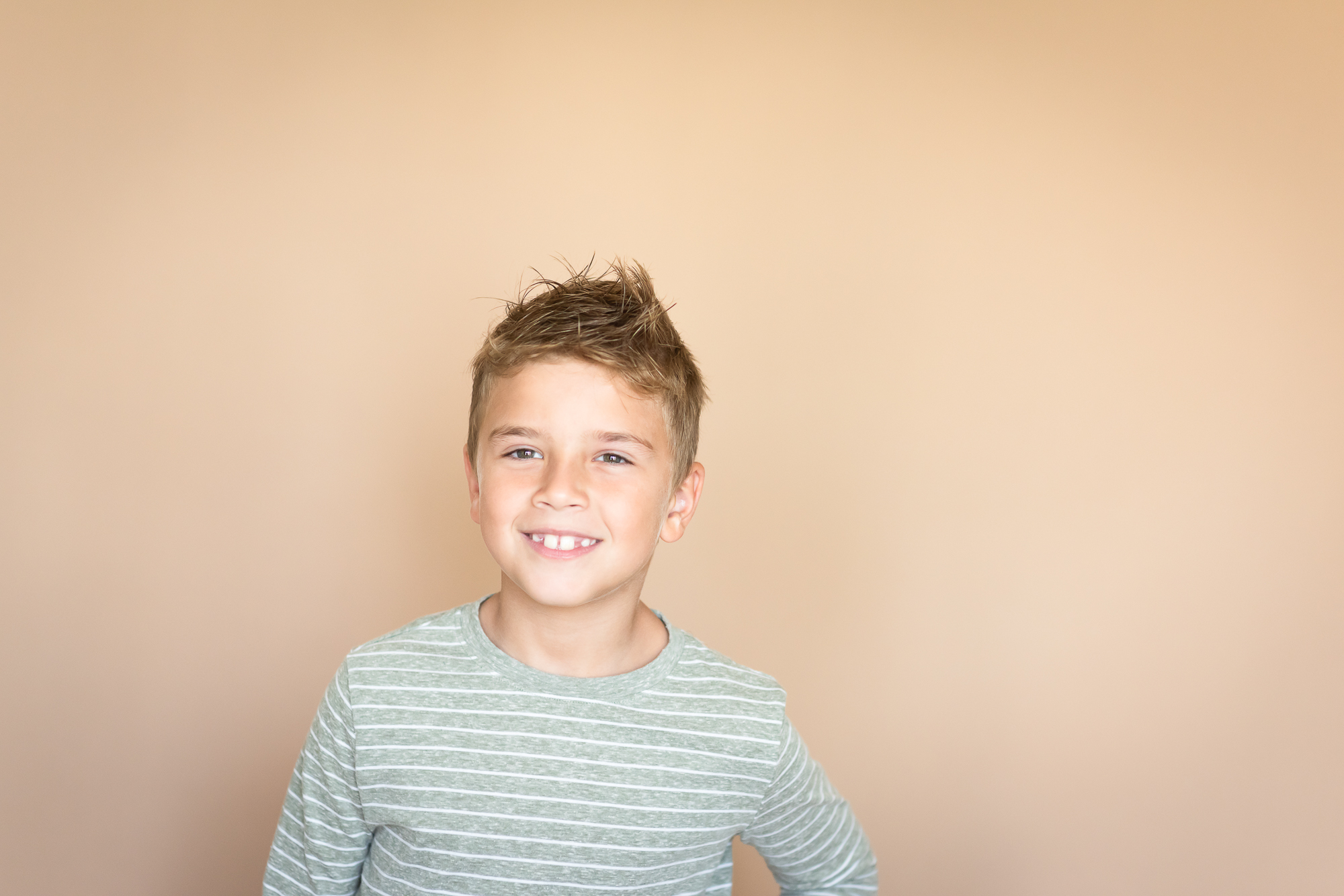 boy in a sage and white striped shirt studio portrait against a tan background showing personality