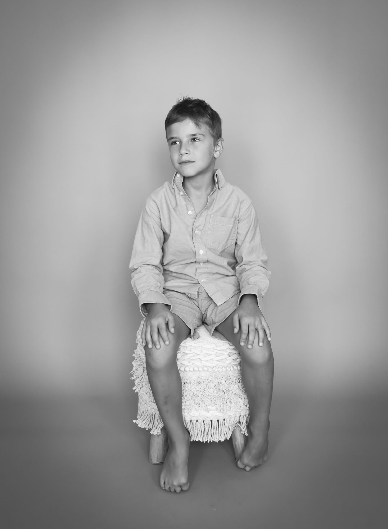 stunning black and white studio portrait of young boy on a boho stool with a timeless feel