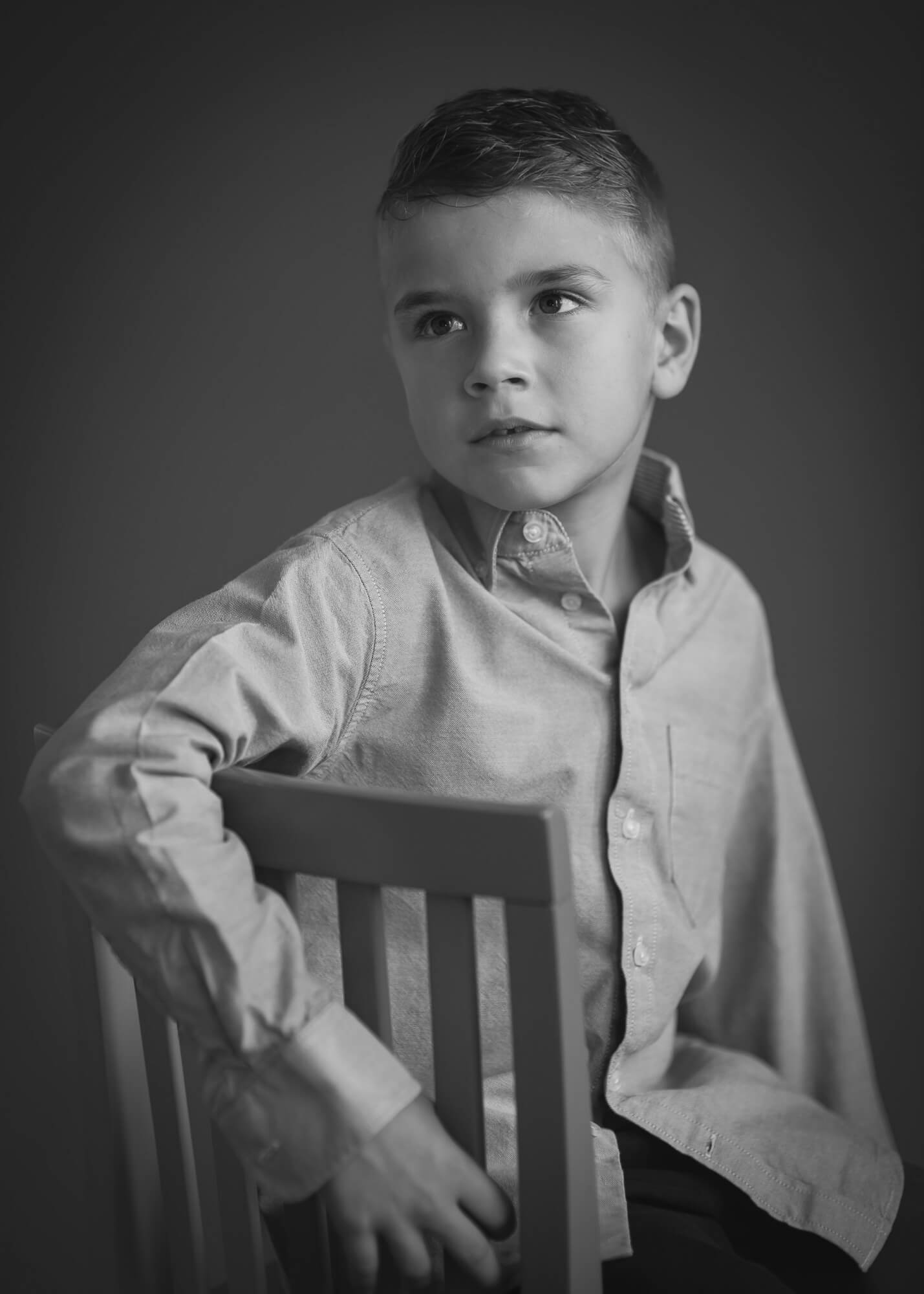 black and white dramatic portrait of a boy looking away wearing a dress shirt with a dark background