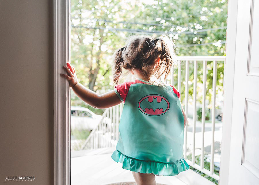 little girl in superwoman cape looking out the door