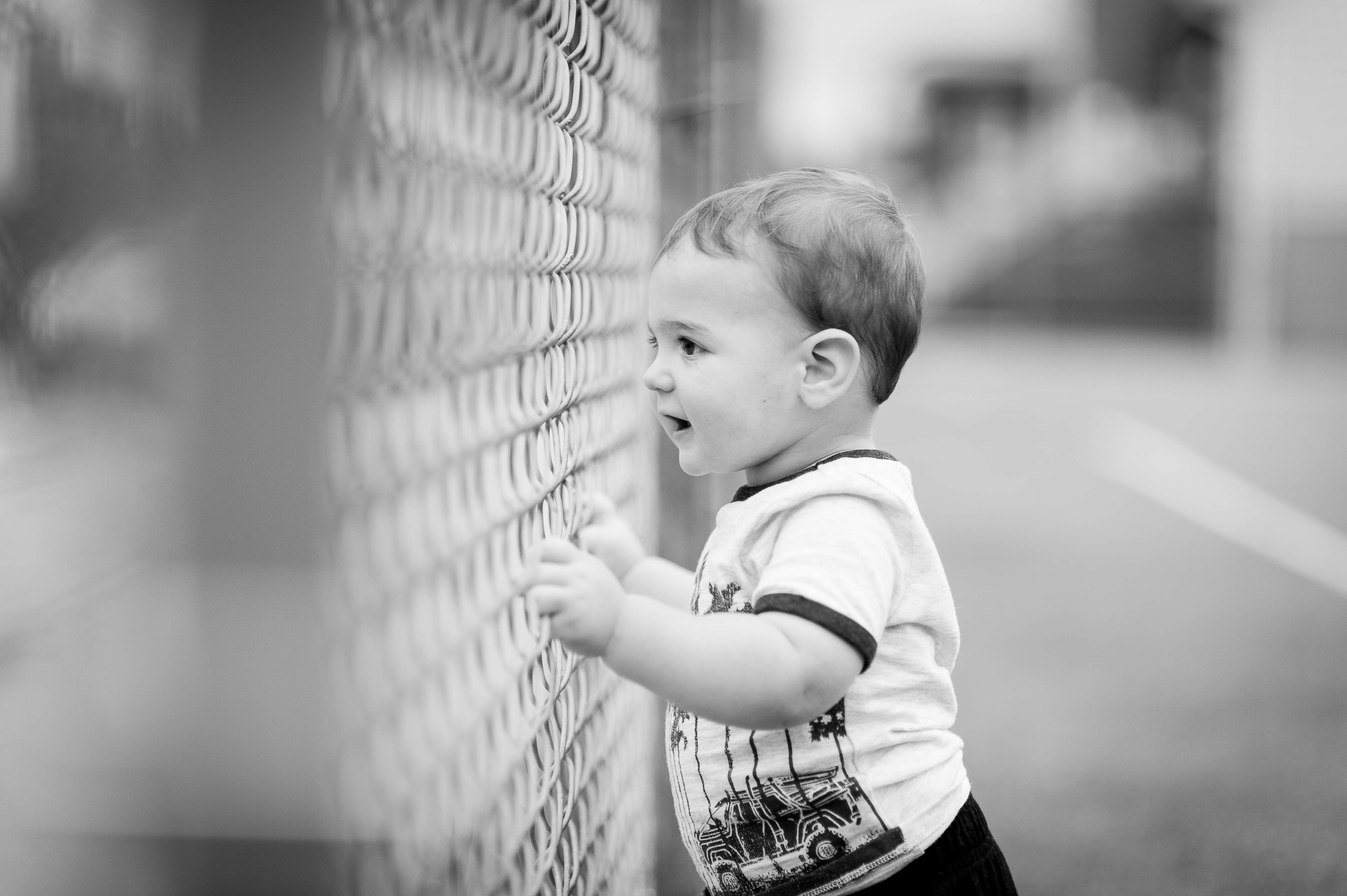 toddler boy looking through chain link fence on playground