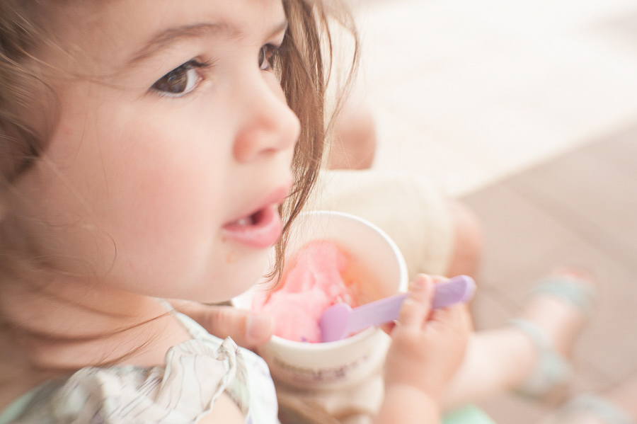 little girl having strawberry ice cream with sprinkles using a purple spoon