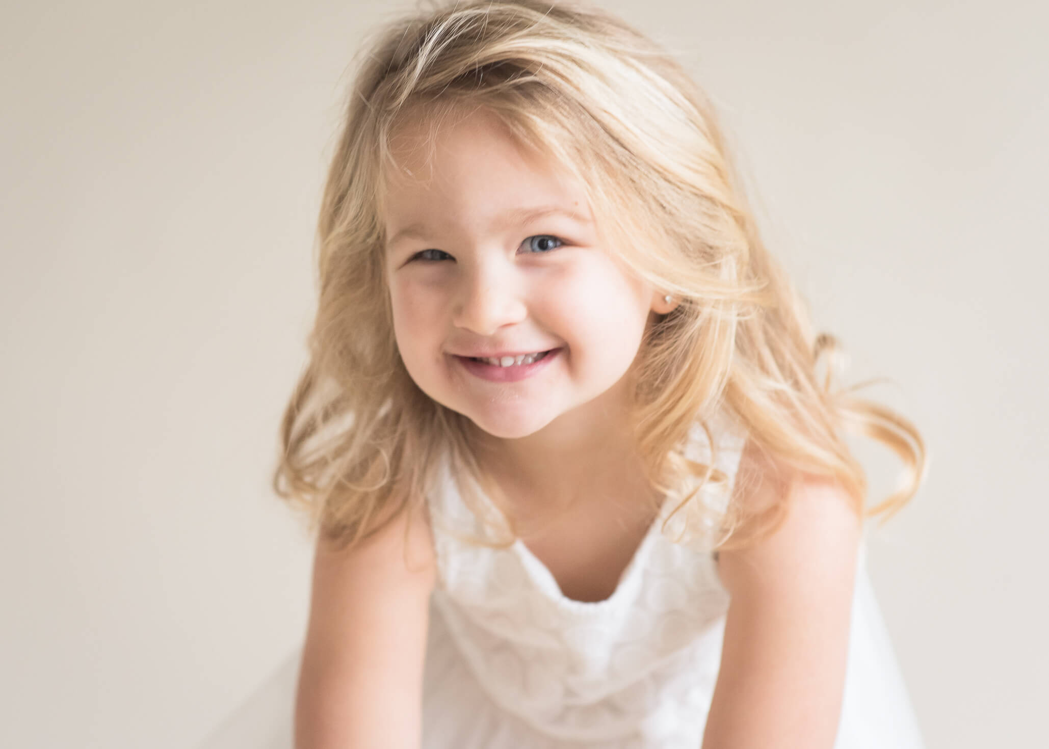 adorable preschooler being spunky and silly in studio session wearing white dress on a light background captured by Allison Amores Photography