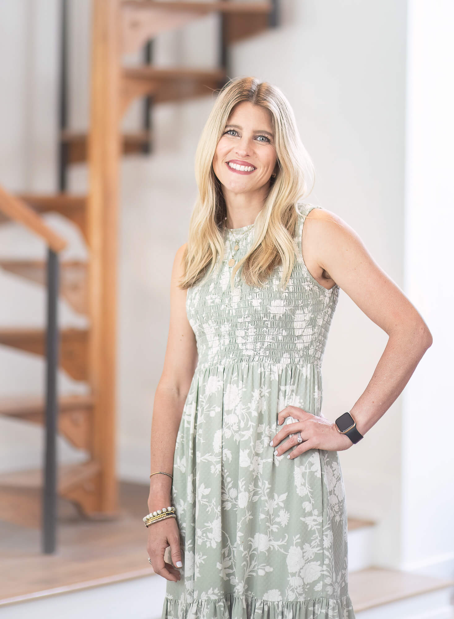 on-location portrait headshot of business owner in a sage green dress with hand on her hip in front of a spiral staircase 
