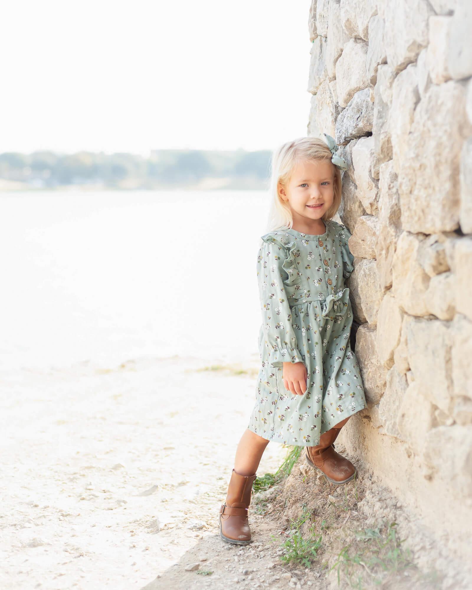 sweet little girl leaning against stone wall by the water in Adriatica Village captured by Allison Amores Photography