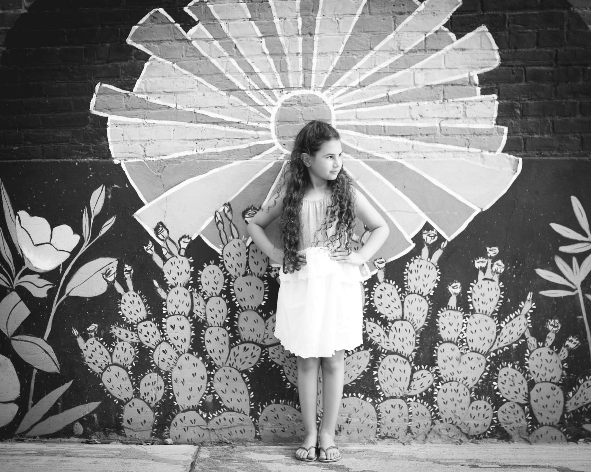 B&W photo of a young girl in Downtown in front of a mural