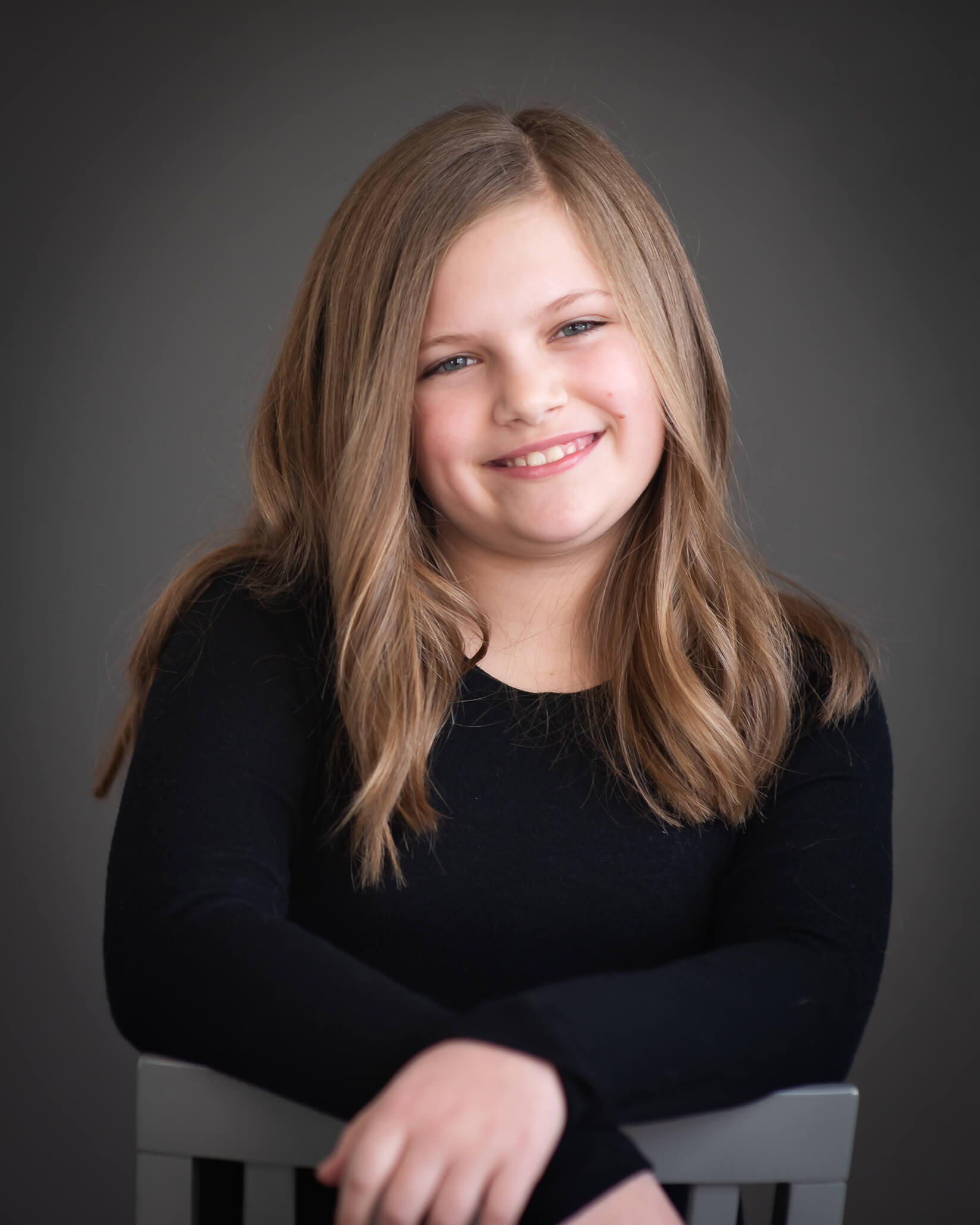 studio color portrait of 10 year old girl sitting backwards on chair & smiling 