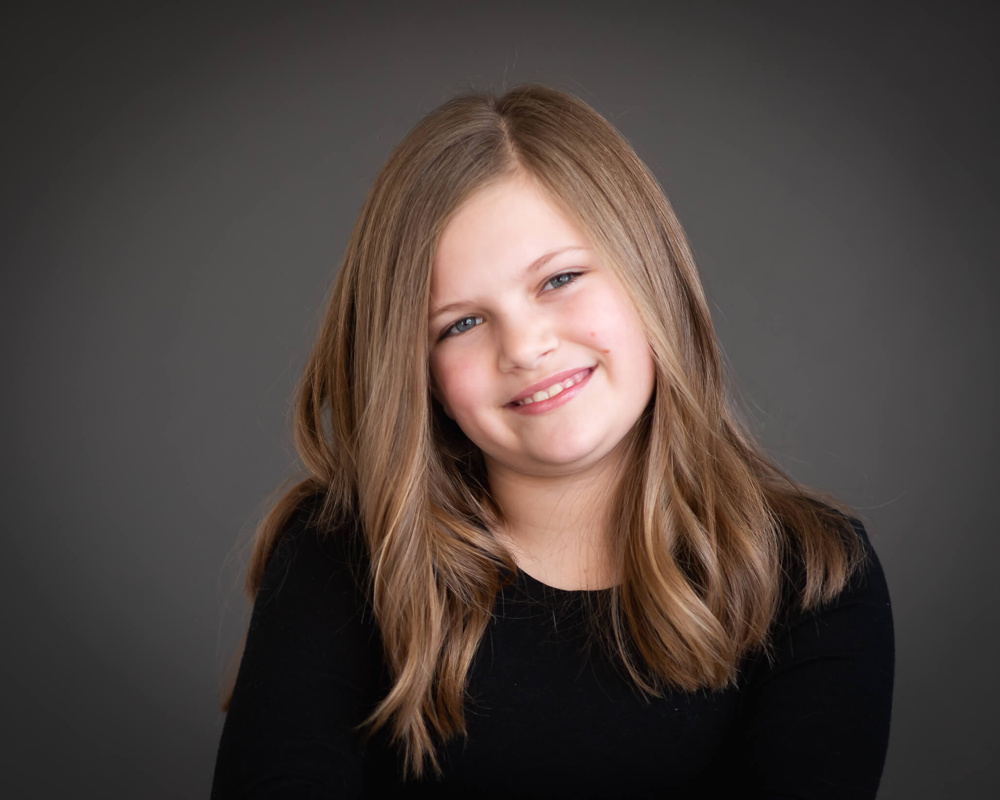 Studio portrait in color of young girl wearing black on a grey background smiling