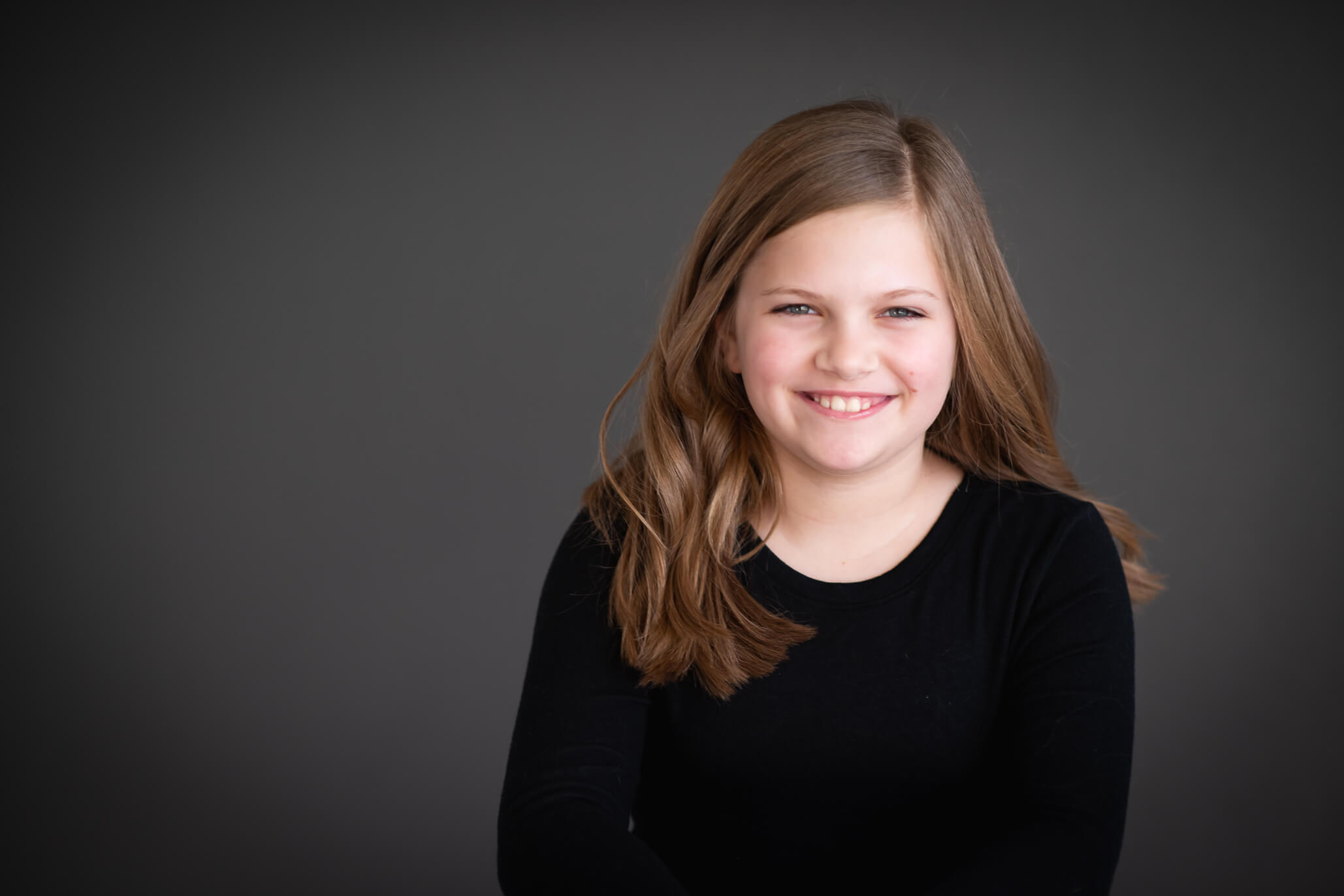 color studio portrait on grey backdrop of elementary aged girl with dark blonde hair wearing a black shirt