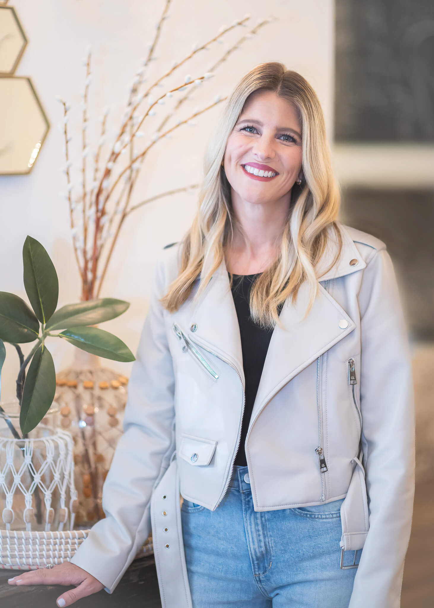 on-location headshot portrait of blonde woman wearing light colored leather jacket next to a console table with plants on it