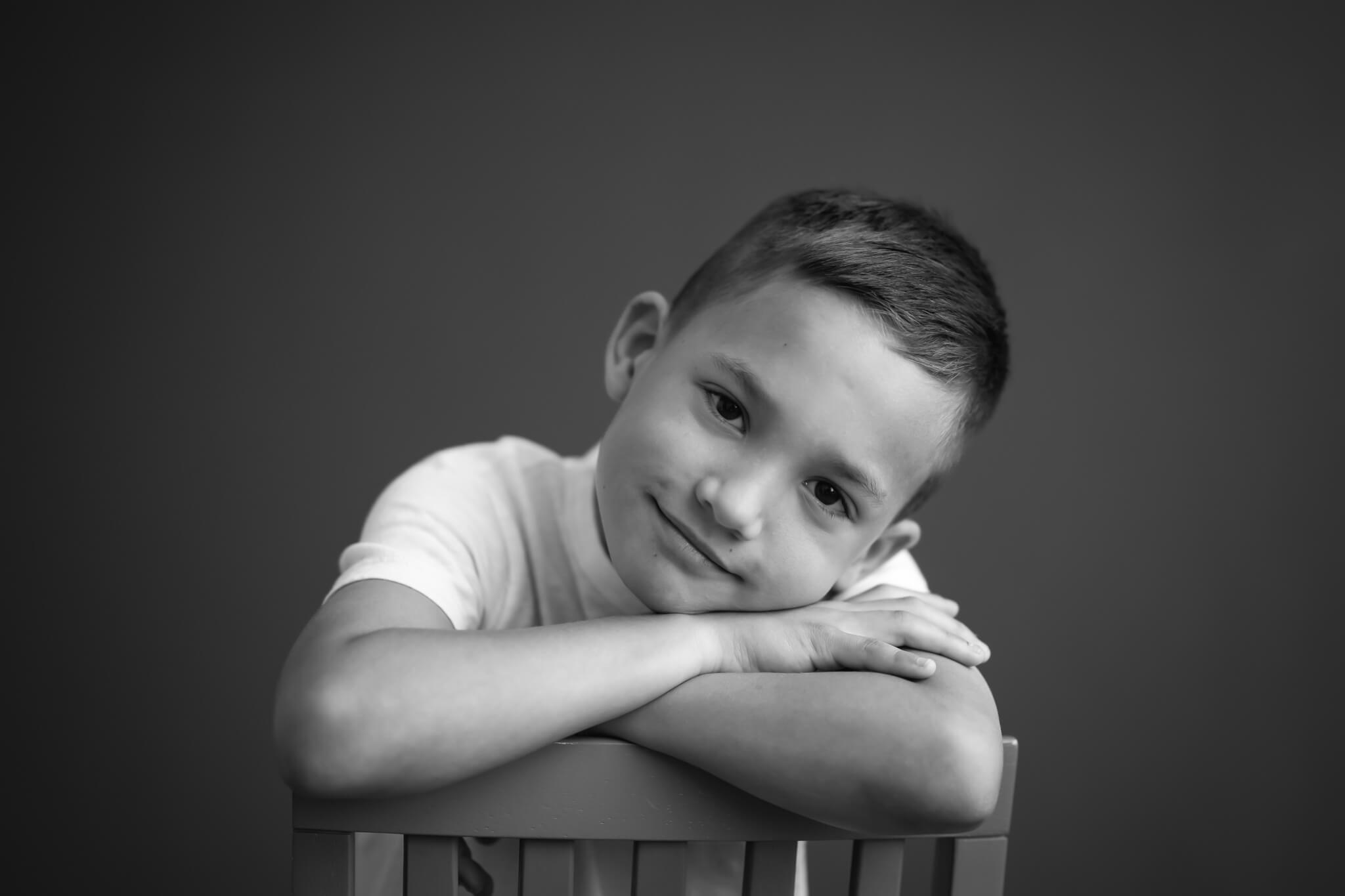 8 year old boy in black and white studio portrait leaning over hair back with arms crossed and head down