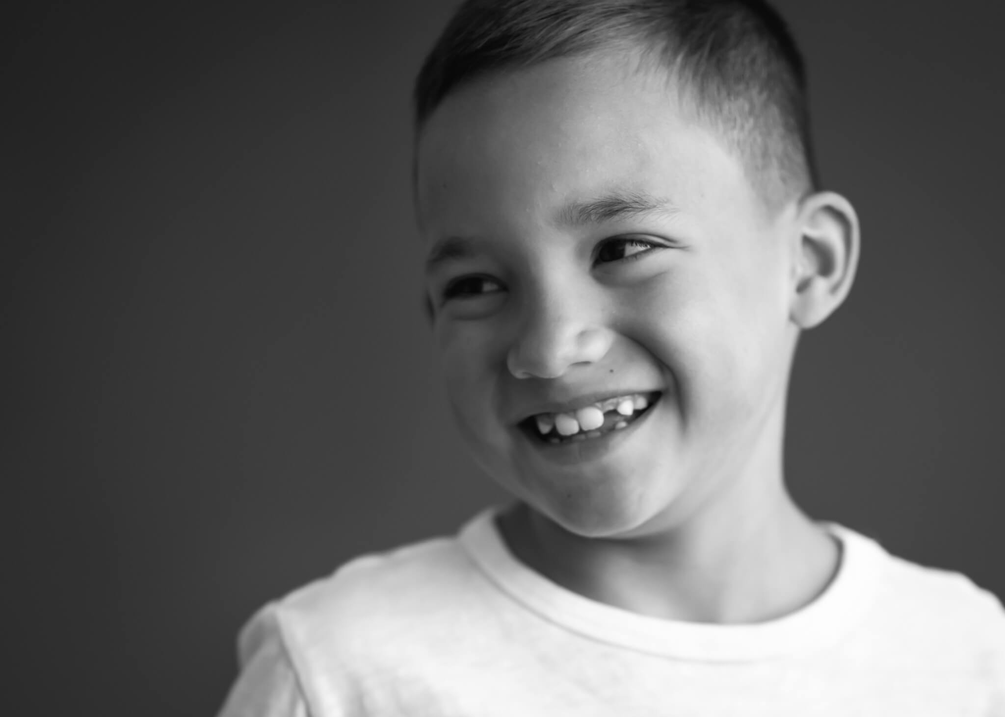 black and white portrait close up of boy laughing in studio, looking away