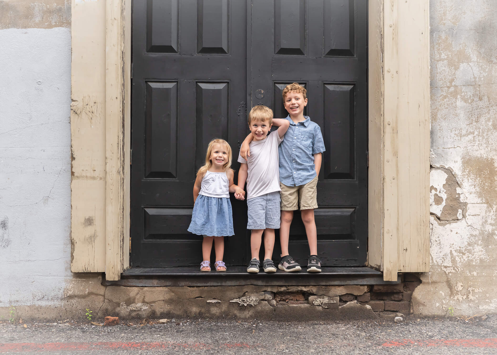 adorable children wearing blue white and tan in front of rustic black door in Downtown McKinney