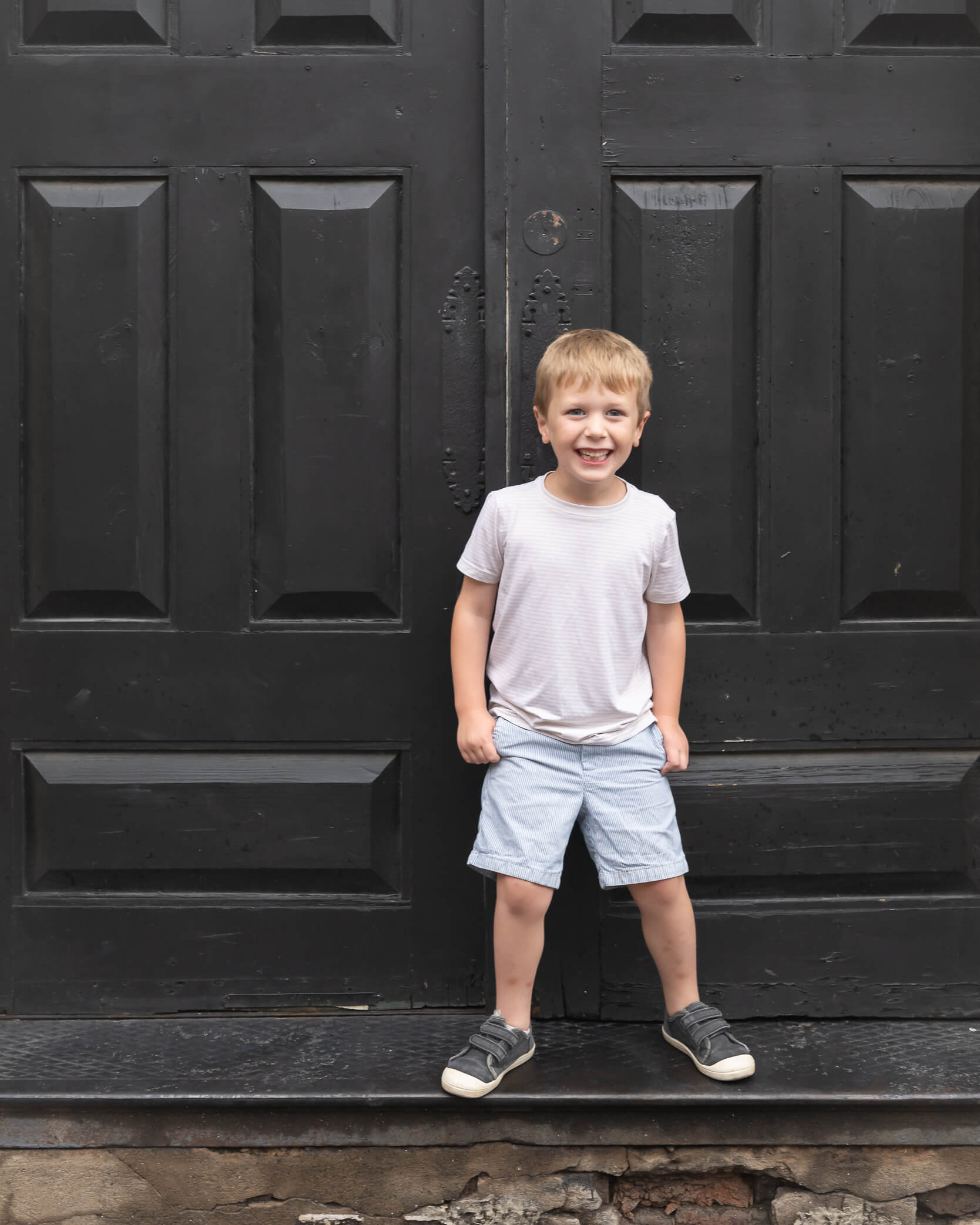 adorable little boy wearing light blue and tan in front of black door in Downtown McKinney during a family photo session