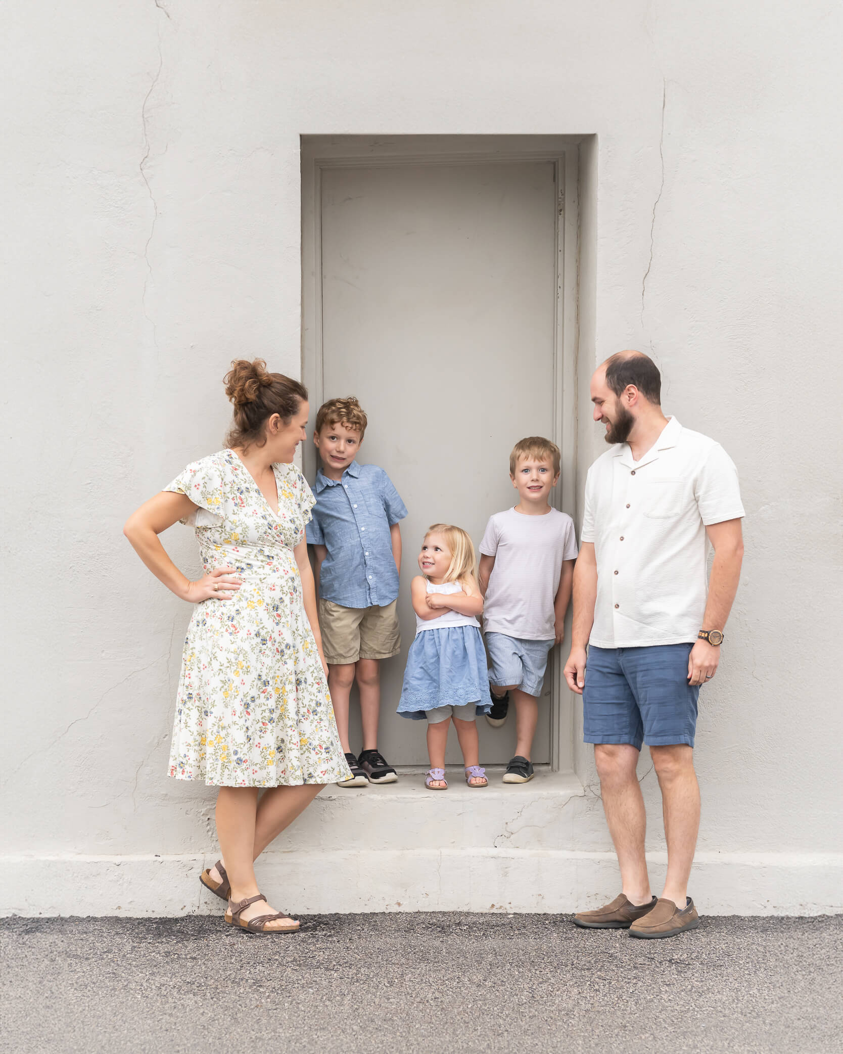 adorable family with 3 small kids standing up in a doorway on an off-white wall in Downtown McKinney