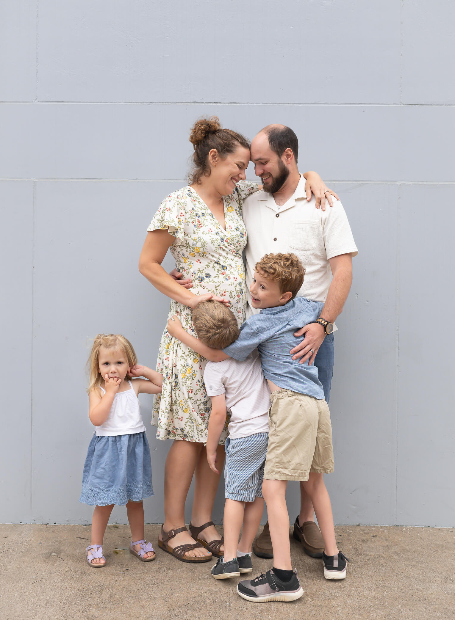 Cutest family with small children in front of a light blue wall being silly in downtown McKinney Texas