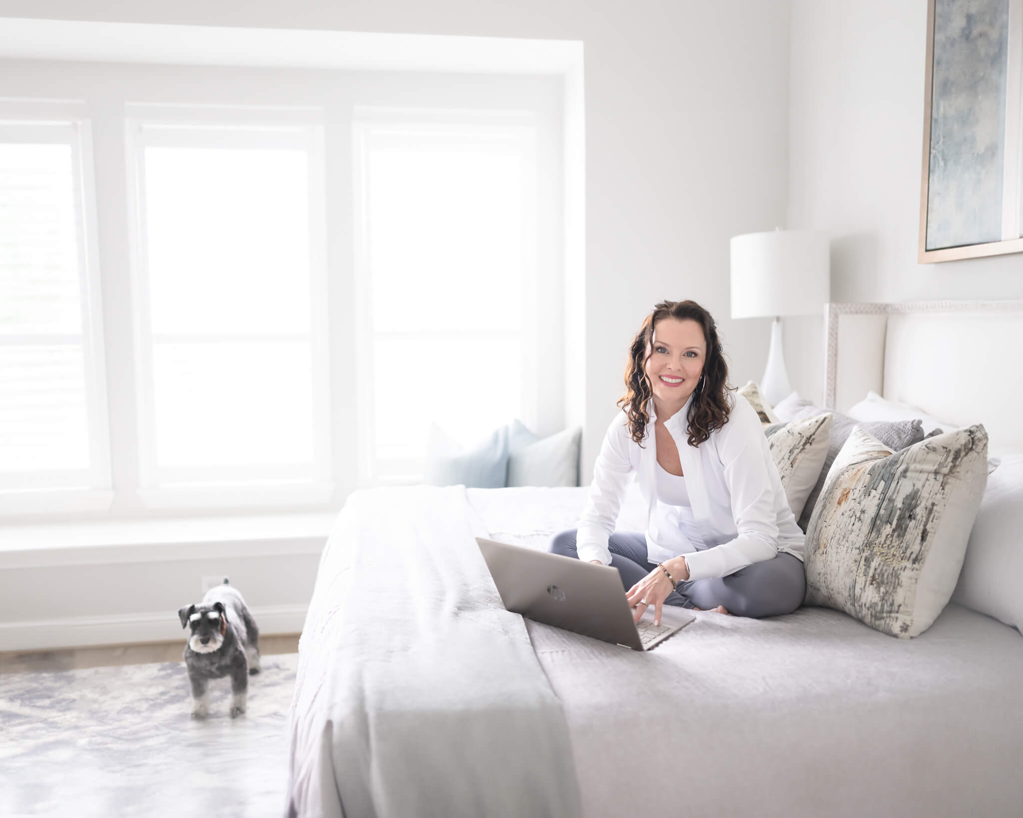 Branding photo of business owner in home working on bed with dog nearby