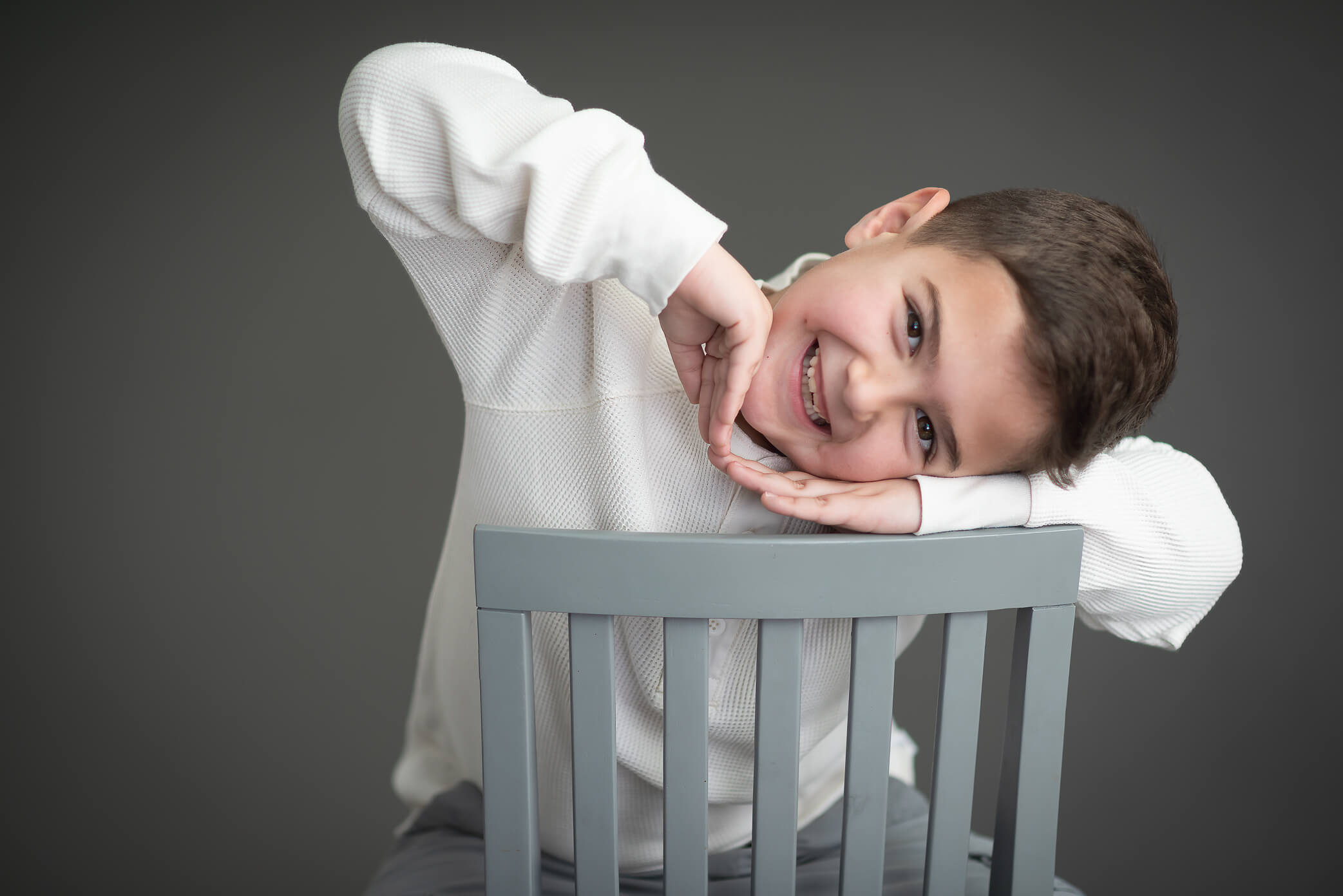 cutest boy being silly in studio session wearing white shirt with grey backdrop during his children's portrait session in mckinney