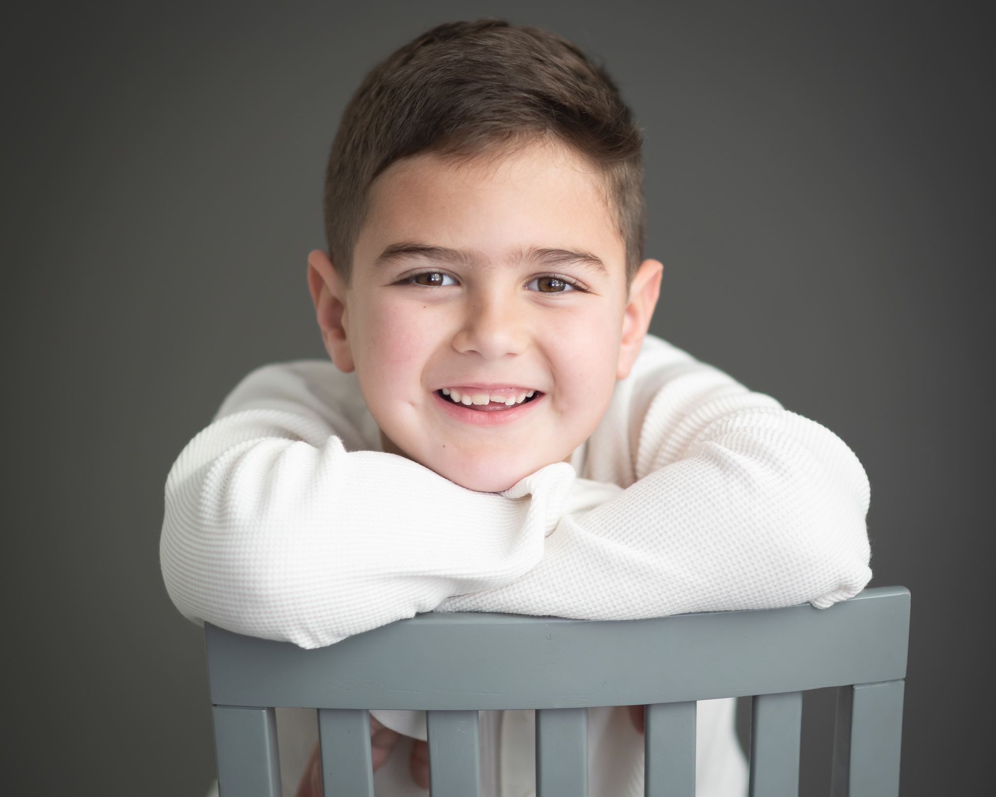 Handsome and adorable boy studio portrait wearing white shirt with grey backdrop