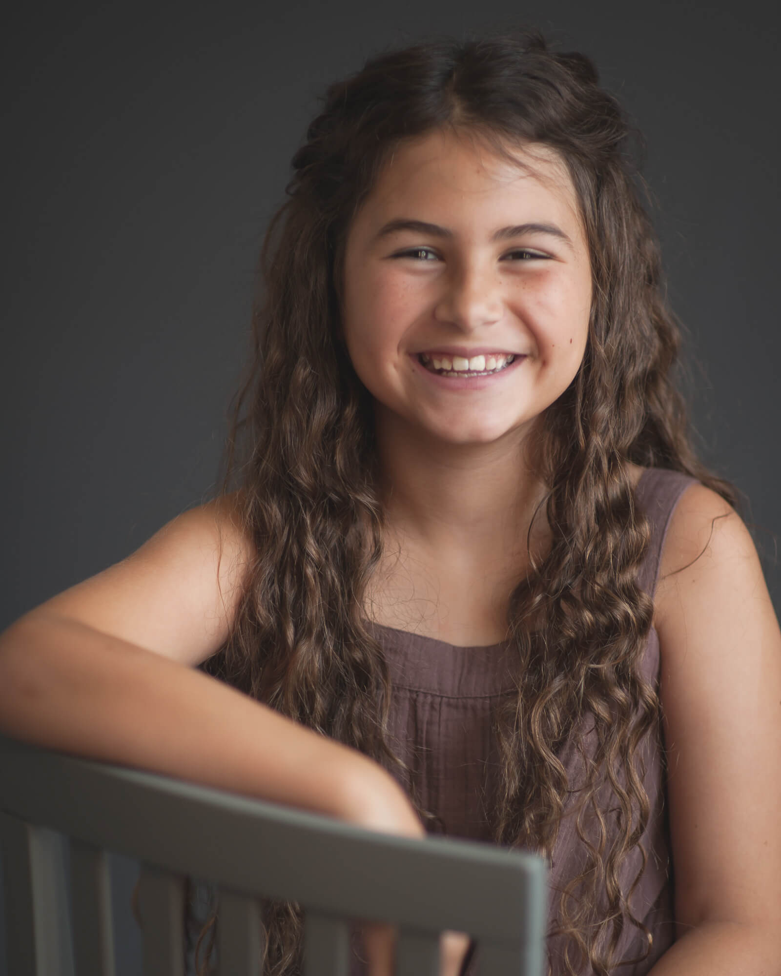 Precious 10 year old girl with long curly hair smiling big in a studio portrait