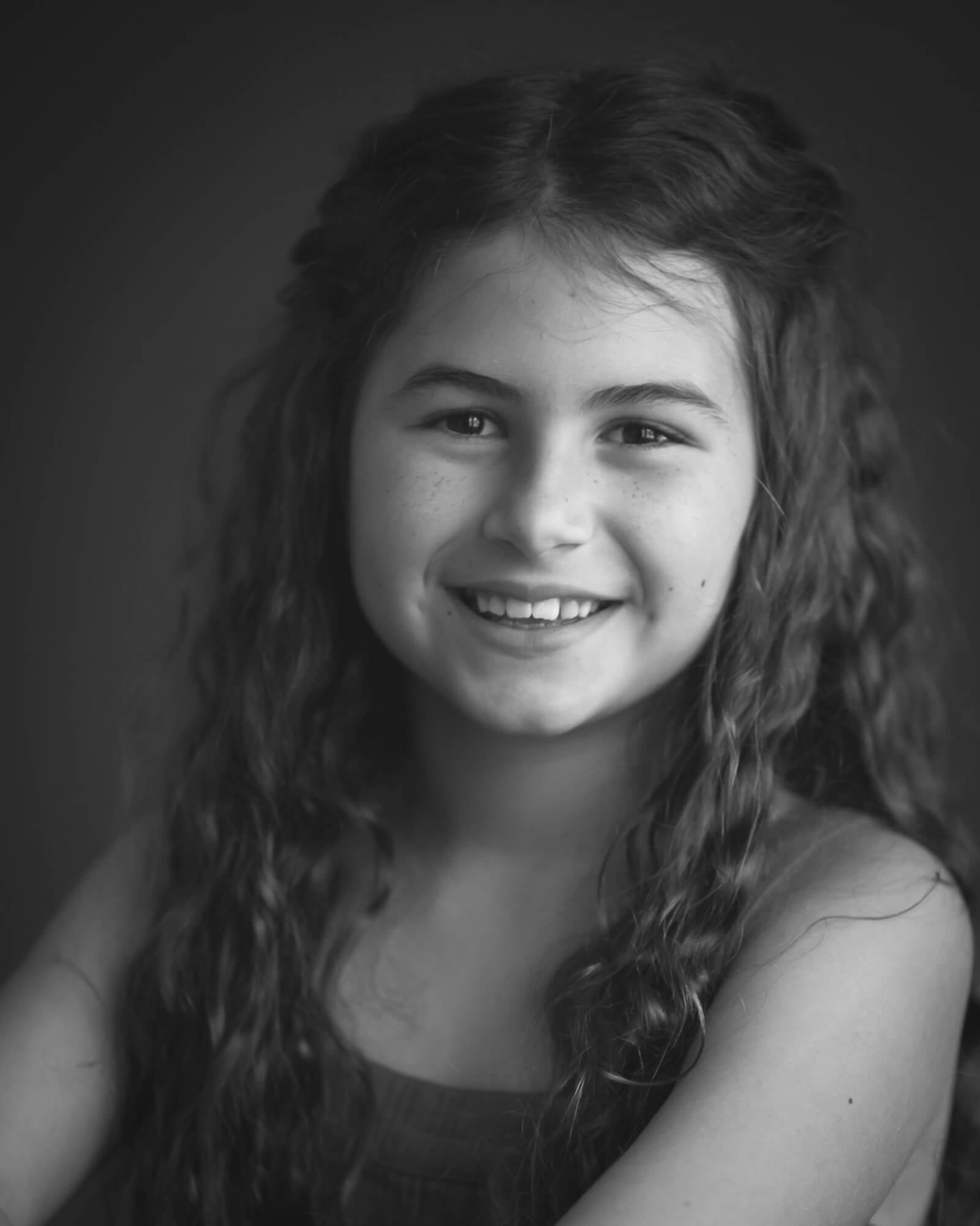 black and white studio portrait of 10 year old smiling girl with long curly hair