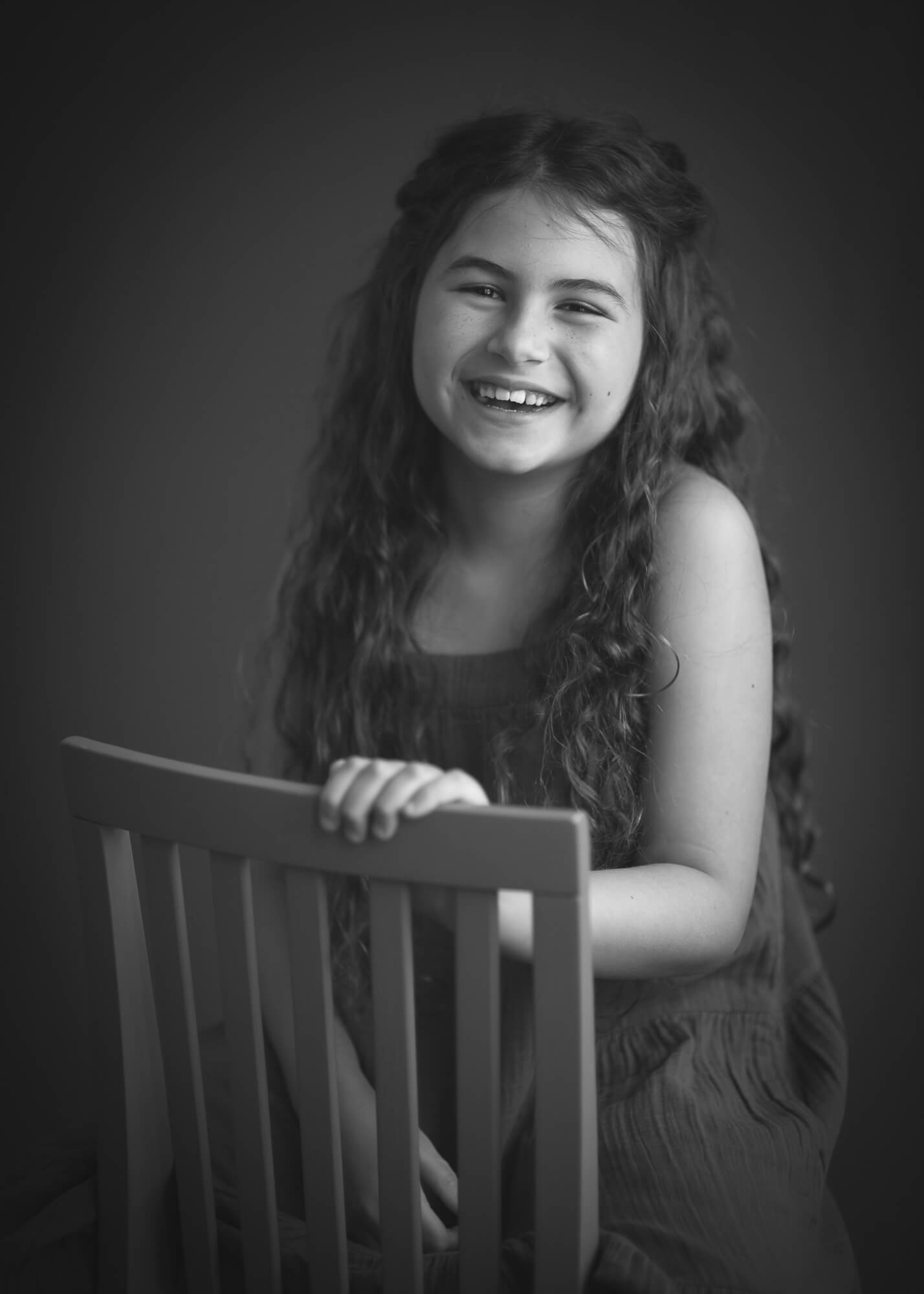 black and white studio portrait of 10 year old girl on a chair smiling