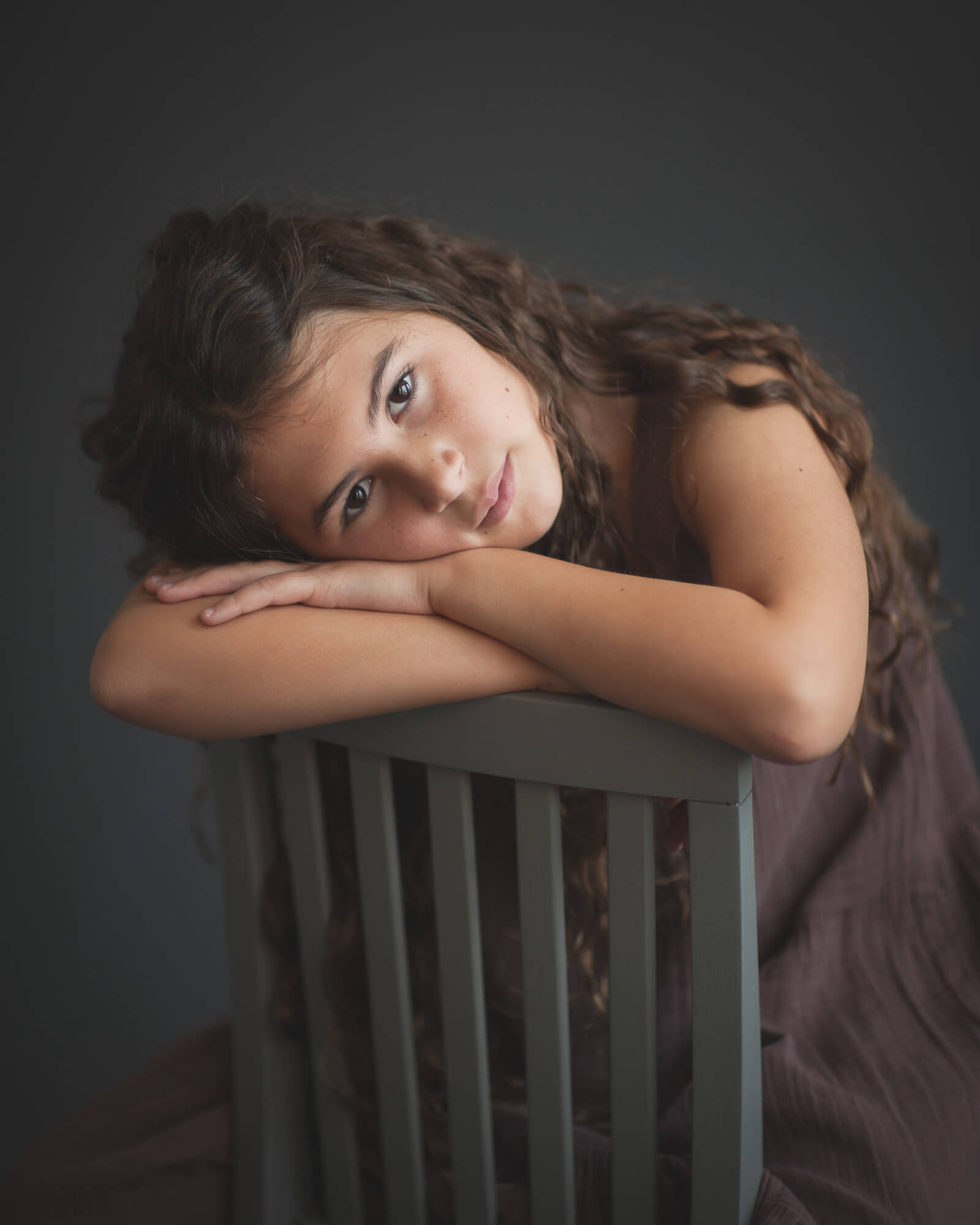 beautiful studio portrait of girl resting head on back of chair