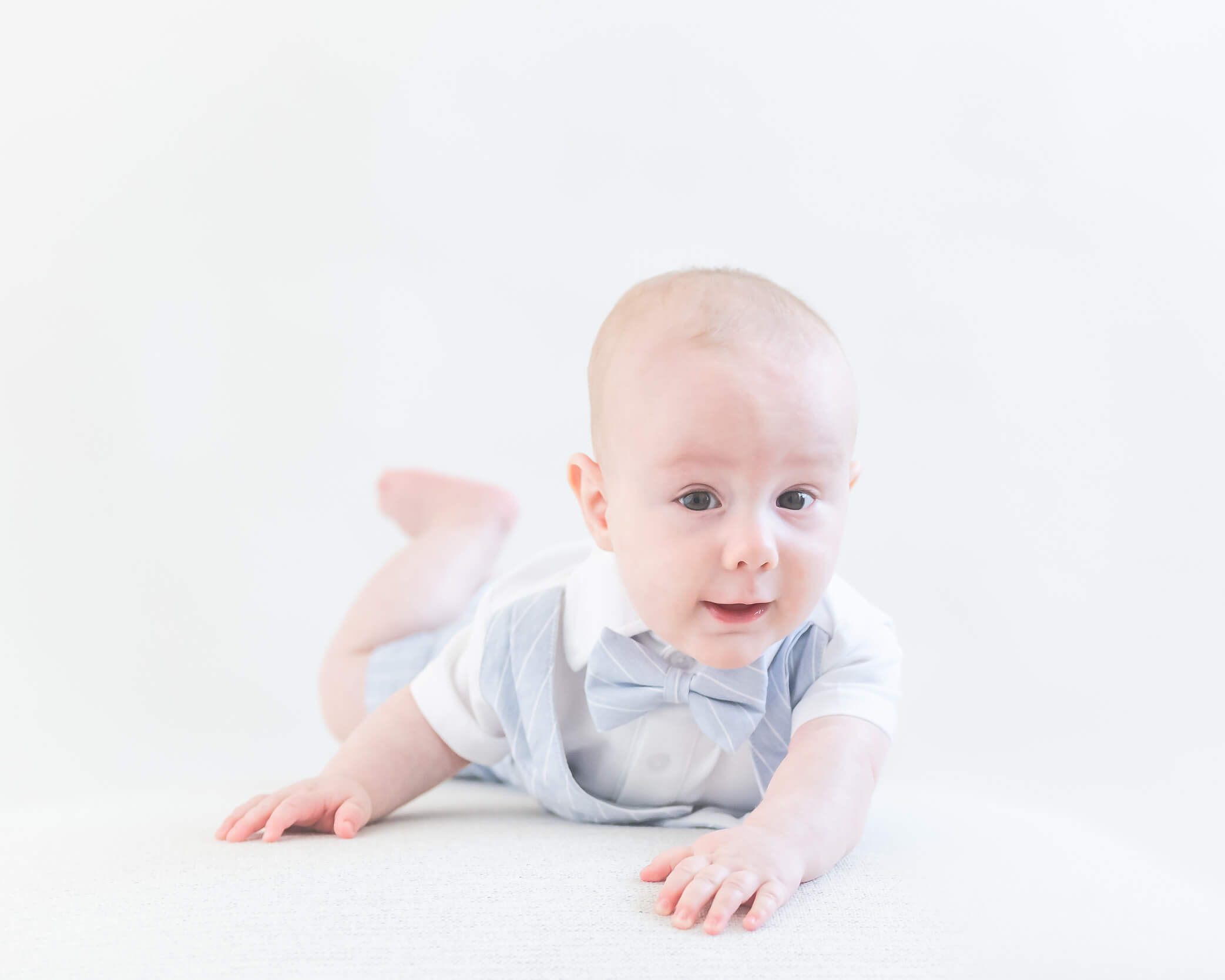 adorable baby boy in light blue and white on his tummy in a light and airy setting