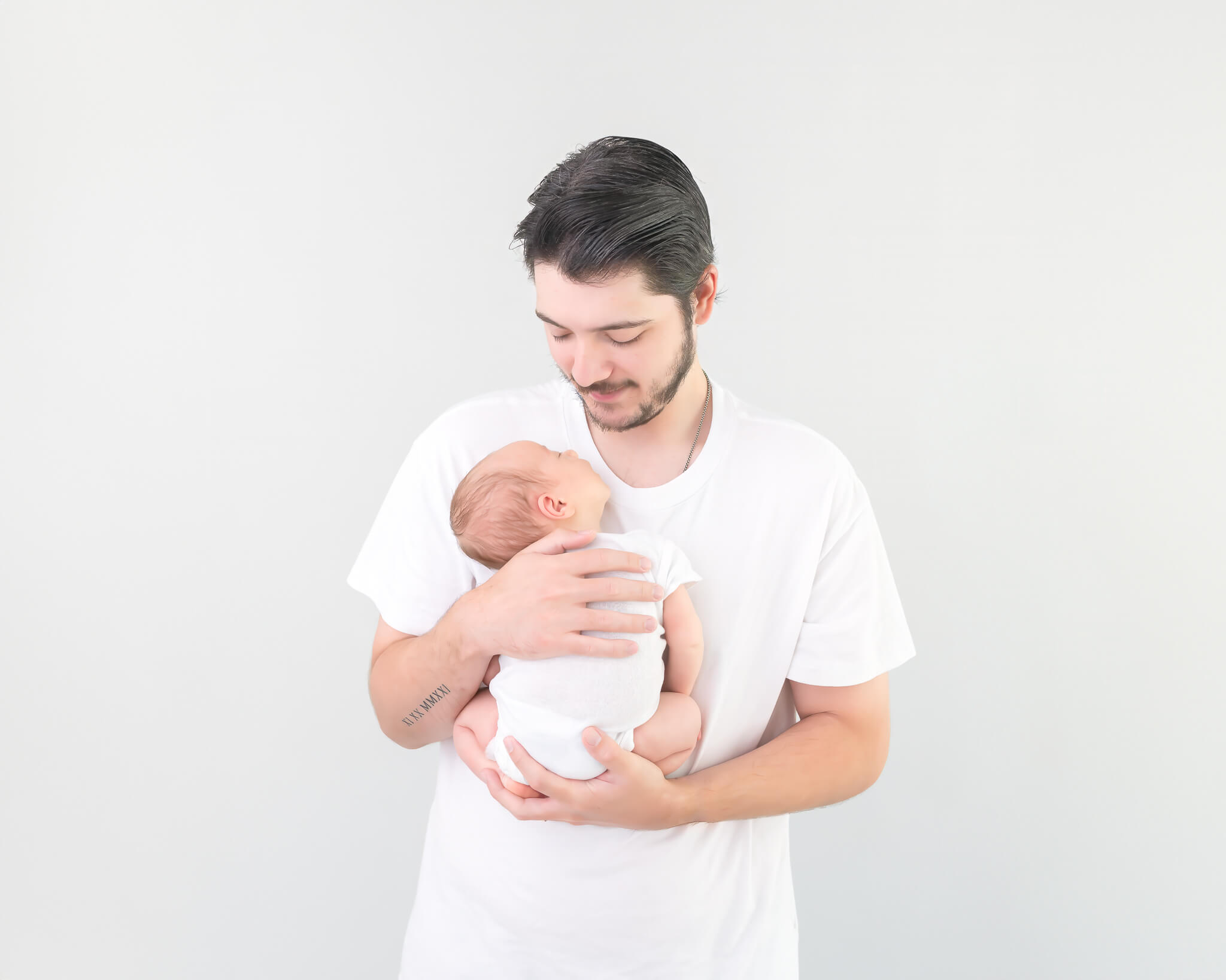 dad looking down at his new baby in timeless studio portrait in white