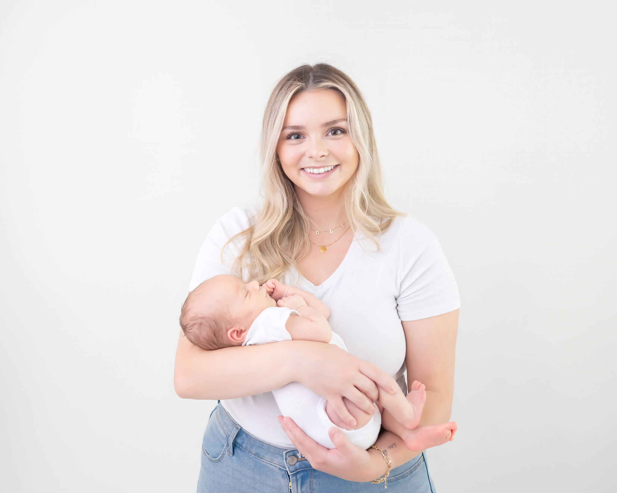 New mom with tiny newborn all in white with white backdrop